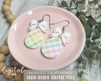 A pair of handmade Easter-themed earrings displayed on a pink plate. The earrings feature a pastel plaid teardrop-shaped charm hanging from a white bow-shaped topper, attached with metal hooks. The background includes greenery and branding for "Brown Cow Creatives." A watermark indicates that this is a digital download for a laser-cut file.